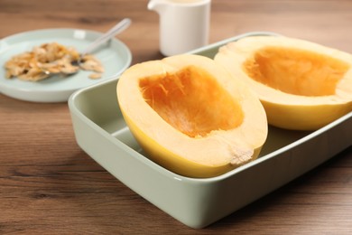 Photo of Raw spaghetti squash halves in baking dish on wooden table, closeup