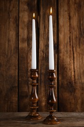 Photo of Elegant candlesticks with burning candles on wooden table
