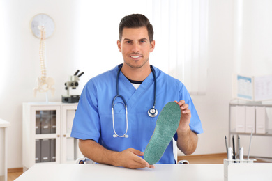 Photo of Handsome male orthopedist showing insole in clinic