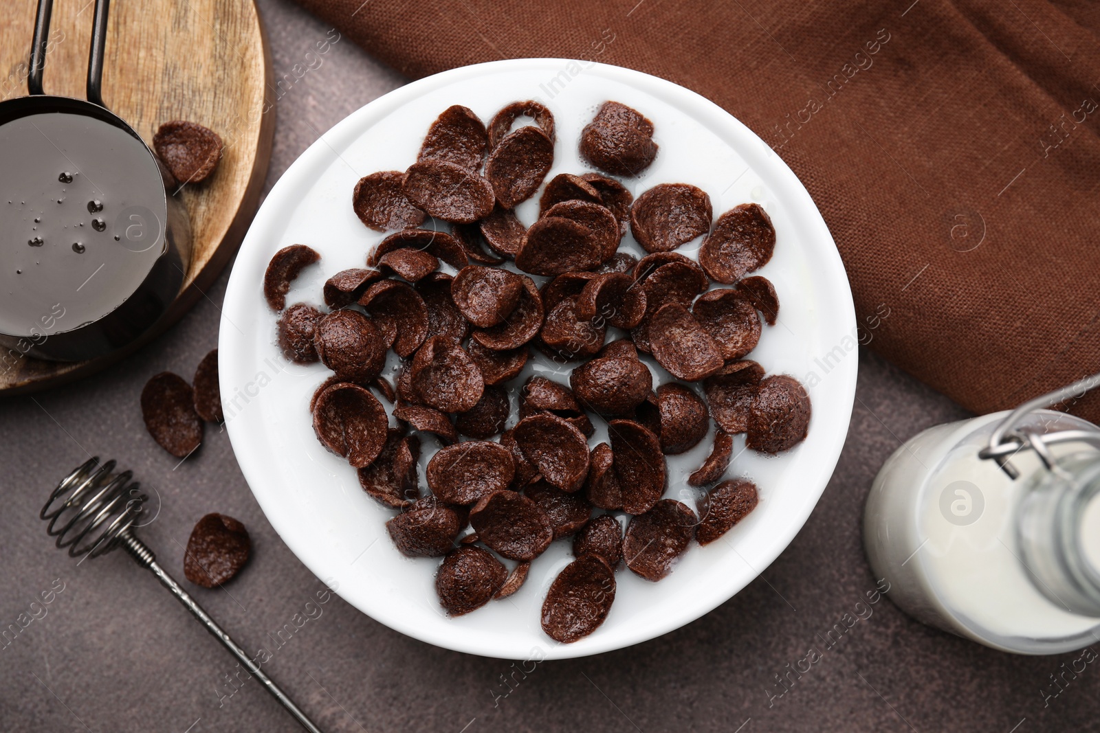 Photo of Breakfast cereal. Chocolate corn flakes and milk in bowl on brown table, flat lay