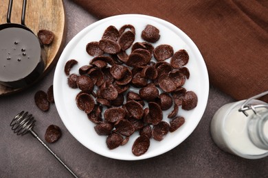 Photo of Breakfast cereal. Chocolate corn flakes and milk in bowl on brown table, flat lay