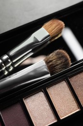 Beautiful eye shadow palette with brushes on grey background, closeup