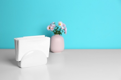 Photo of Ceramic napkin holder with paper serviettes and flowers in vase on table. Space for text