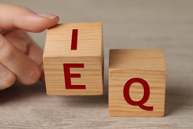 Photo of Woman turning cube with letters E and I near Q at wooden table, closeup