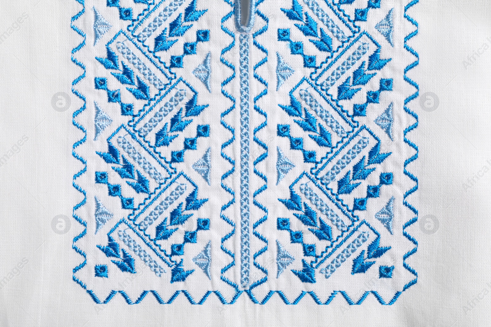 Photo of Beautiful light blue Ukrainian national embroidery on white fabric, top view
