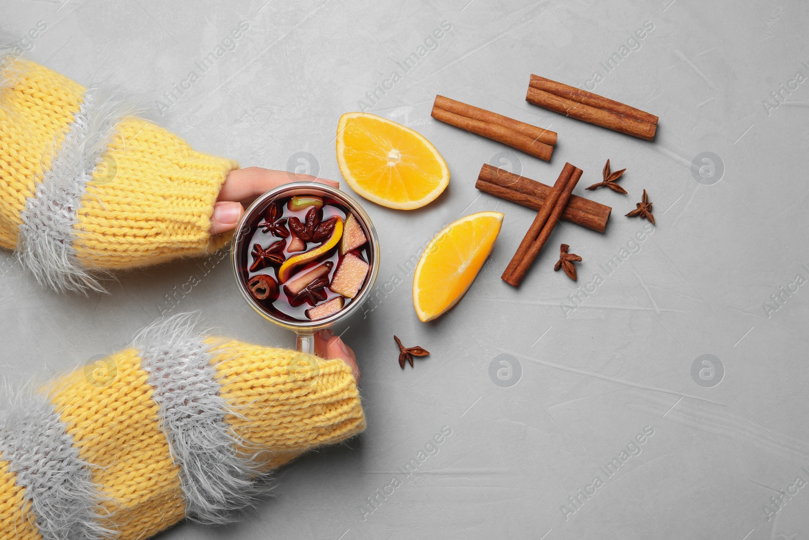 Photo of Woman holding cup with hot mulled wine on table, top view