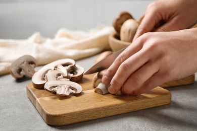 Photo of Woman cutting fresh wild mushrooms at light grey table, closeup
