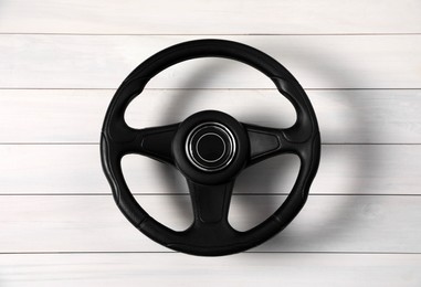 Photo of New black steering wheel on white wooden table, top view
