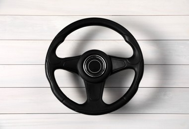 New black steering wheel on white wooden table, top view