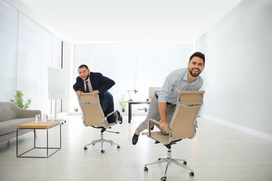 Happy office employees riding chairs at workplace