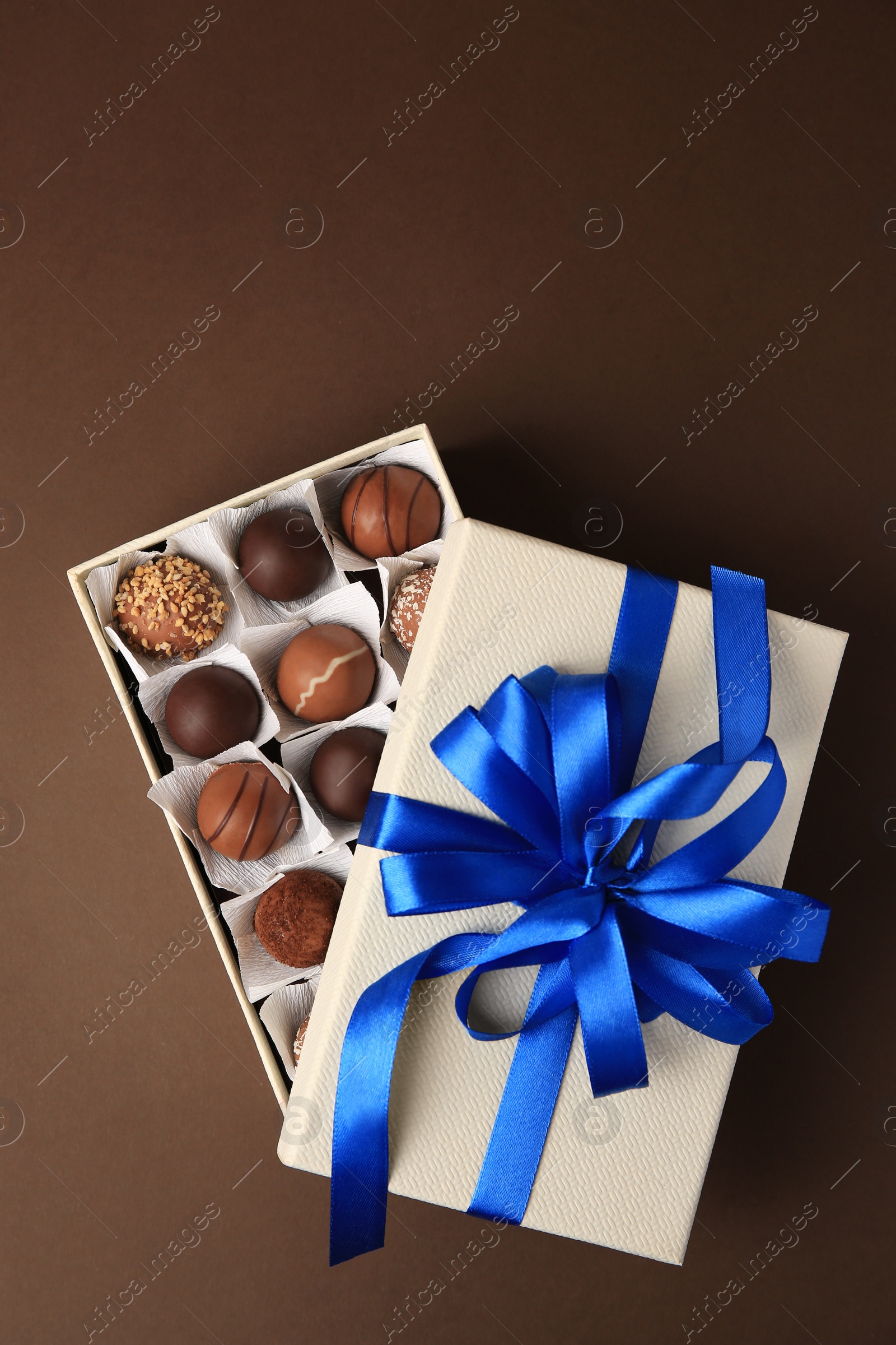 Photo of Box with delicious chocolate candies on brown background, top view