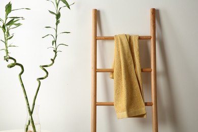 Photo of Yellow towel on wooden ladder and houseplant indoors