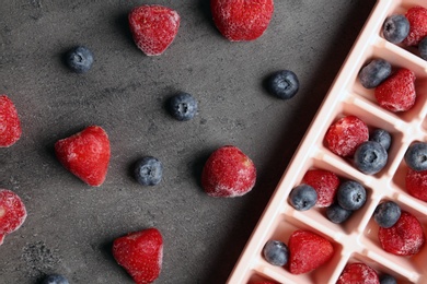 Photo of Flat lay composition with ice cube tray and frozen berries on grey background
