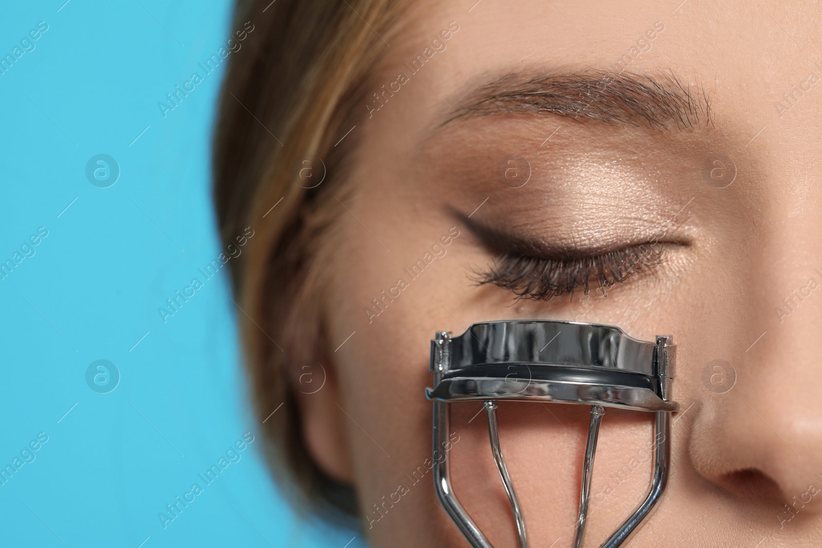 Photo of Young woman with eyelash curler on light blue background, closeup