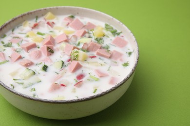 Photo of Delicious cold summer soup (okroshka) with boiled sausage in bowl on green table, closeup. Space for text