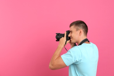 Photo of Young professional photographer taking picture on pink background. Space for text