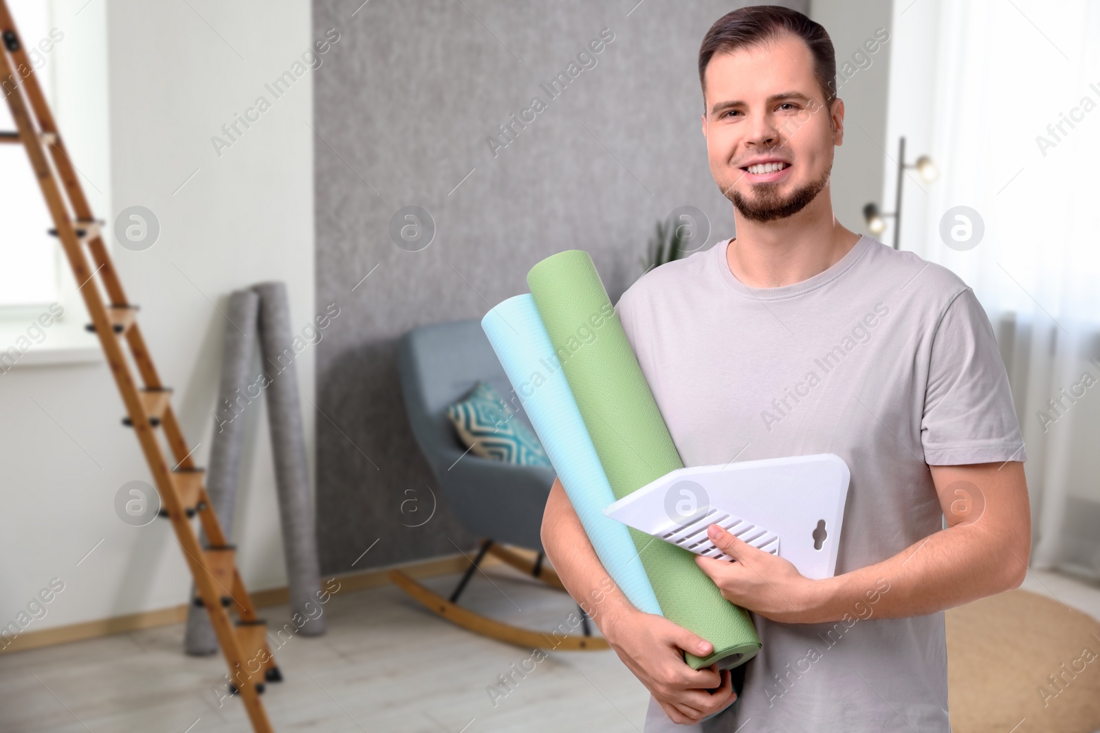 Image of Man with wallpaper rolls and smoothing tool in room