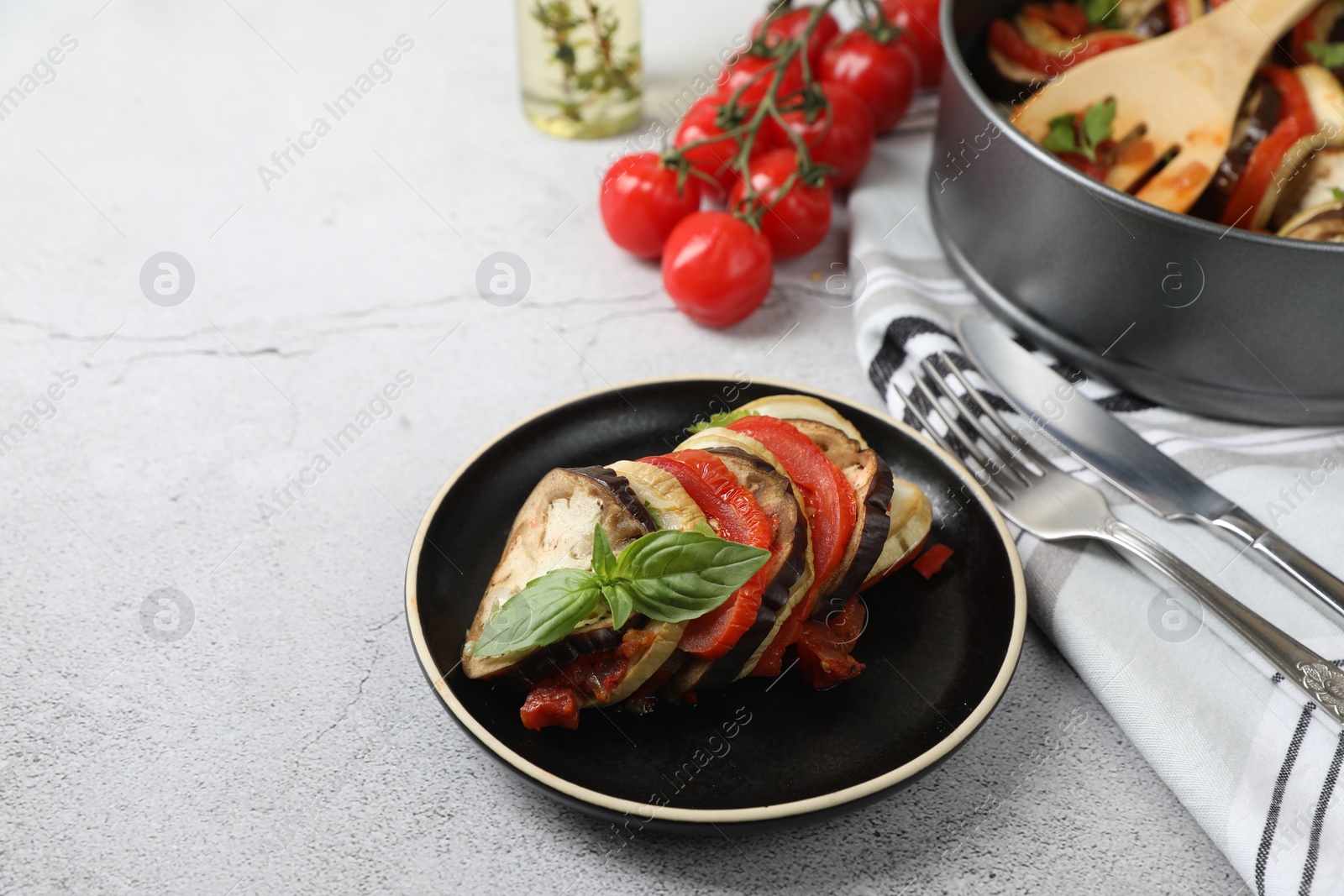 Photo of Delicious ratatouille served with basil on light grey table. Space for text