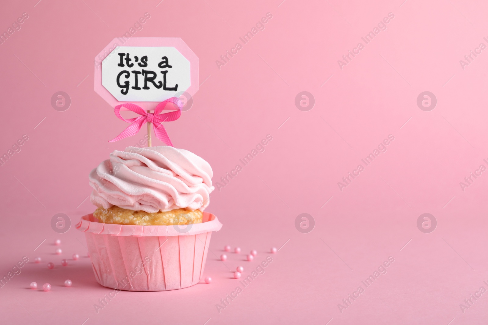 Photo of Beautifully decorated baby shower cupcake with cream and girl topper on pink background. Space for text