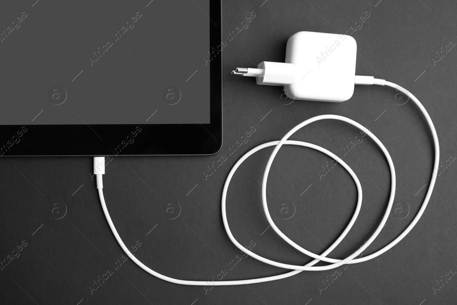 Photo of Tablet and USB charger on black background, flat lay. Modern technology