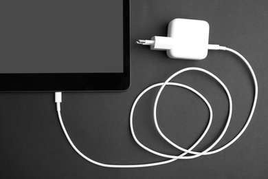 Photo of Tablet and USB charger on black background, flat lay. Modern technology