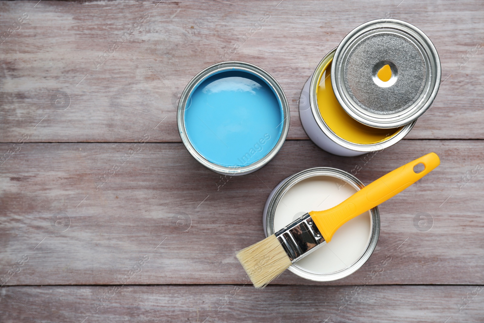 Photo of Cans of colorful paints with brush on wooden table, flat lay. Space for text