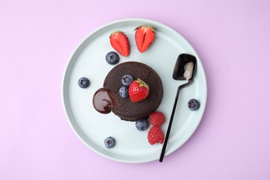 Plate with delicious chocolate fondant and berries on violet table, top view