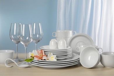 Photo of Glasses and clean dishware with flowers on light grey table