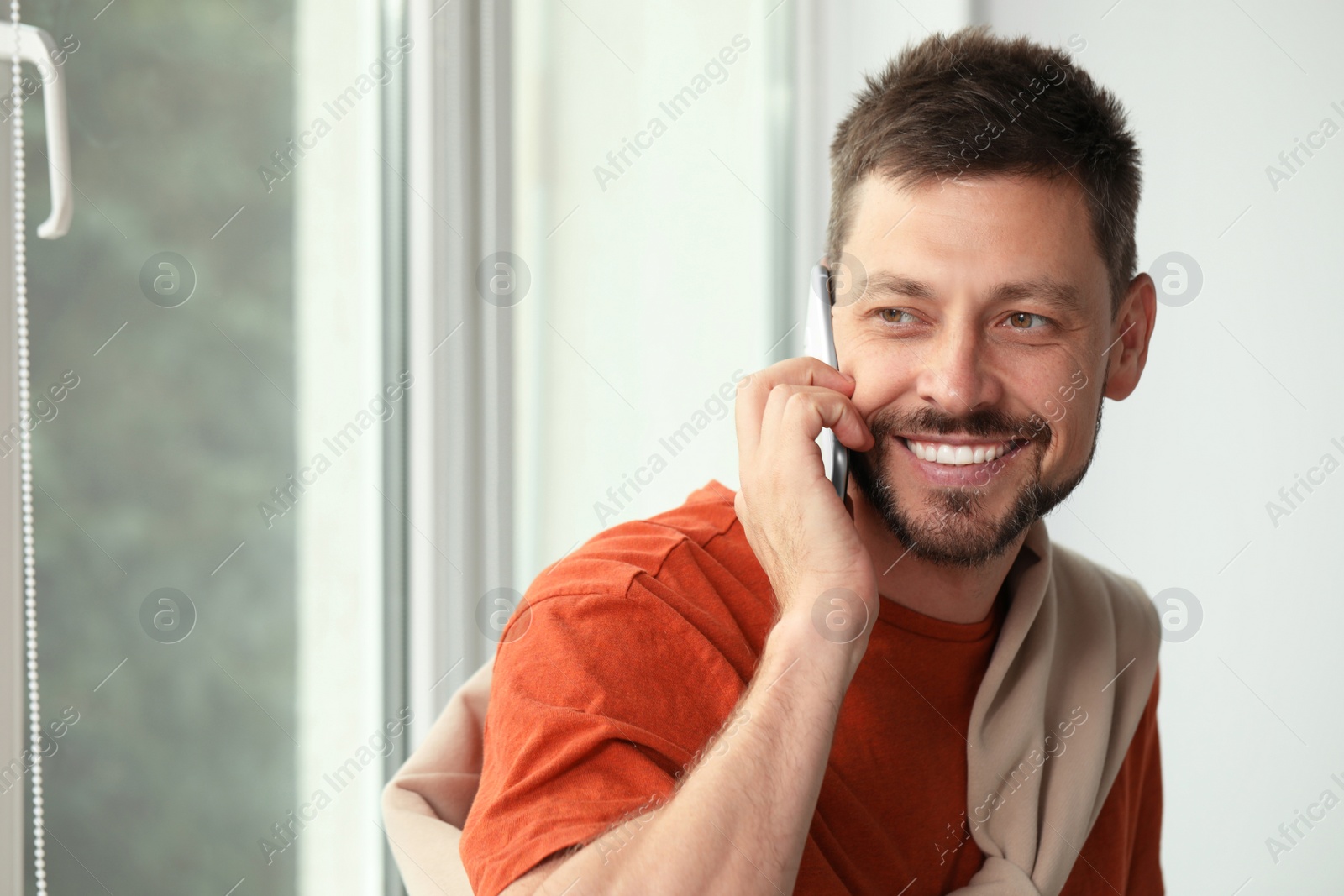 Photo of Happy man talking on smartphone at home, space for text