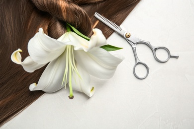 Flat lay composition with brown hair, scissors and flower on gray background