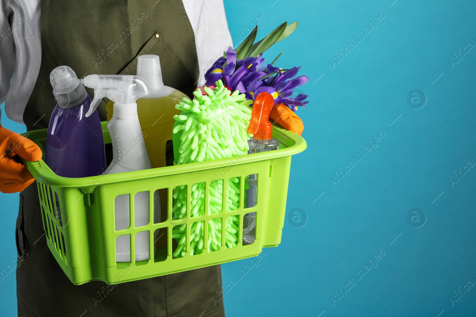 Photo of Spring cleaning. Woman holding basket with detergents, flowers and tools on light blue background, closeup. Space for text
