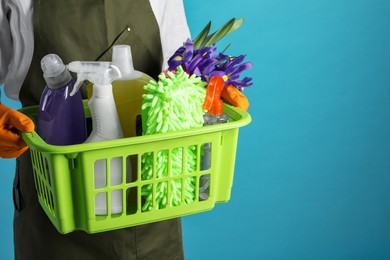 Spring cleaning. Woman holding basket with detergents, flowers and tools on light blue background, closeup. Space for text