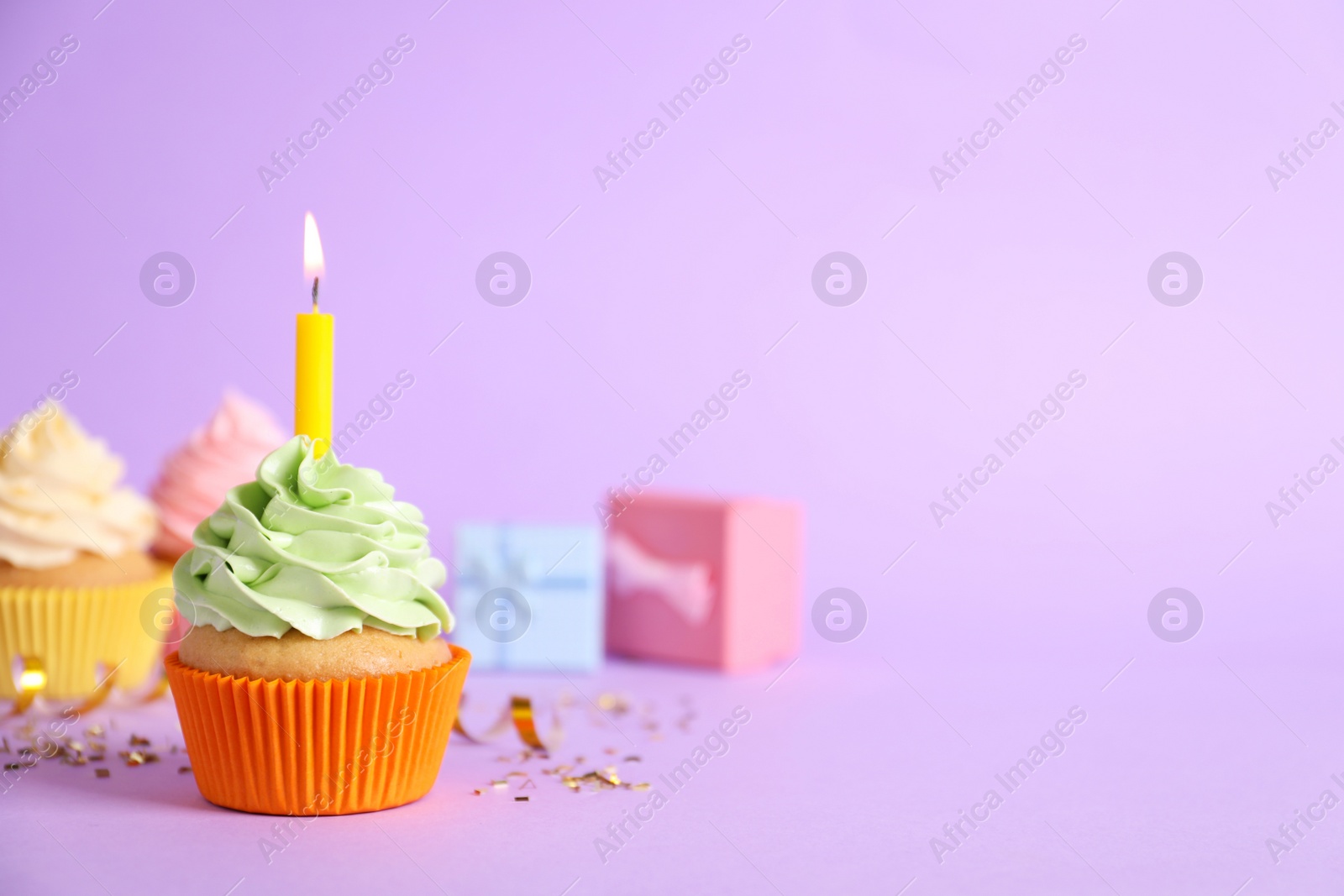 Photo of Birthday cupcake with burning candle and confetti on violet background. Space for text