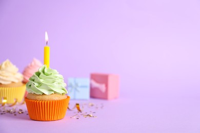 Birthday cupcake with burning candle and confetti on violet background. Space for text