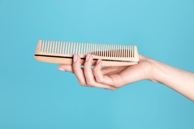 Woman holding wooden hair comb against blue background, closeup