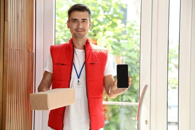 Happy young courier with parcel and mobile phone in doorway
