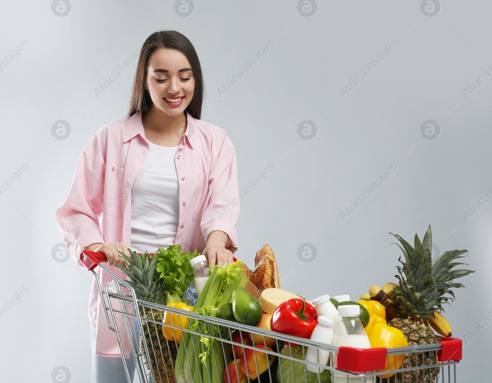 Photo of Young woman with shopping cart full of groceries on grey background