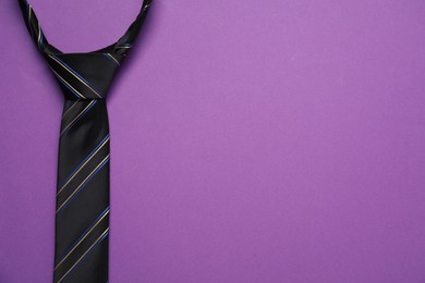 Photo of Striped necktie on purple background, top view. Space for text