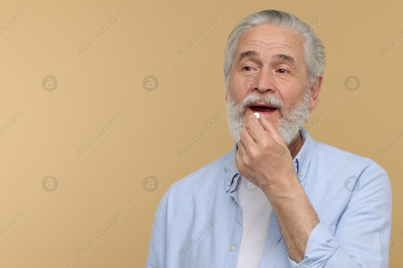 Photo of Senior man taking pill on beige background. Space for text