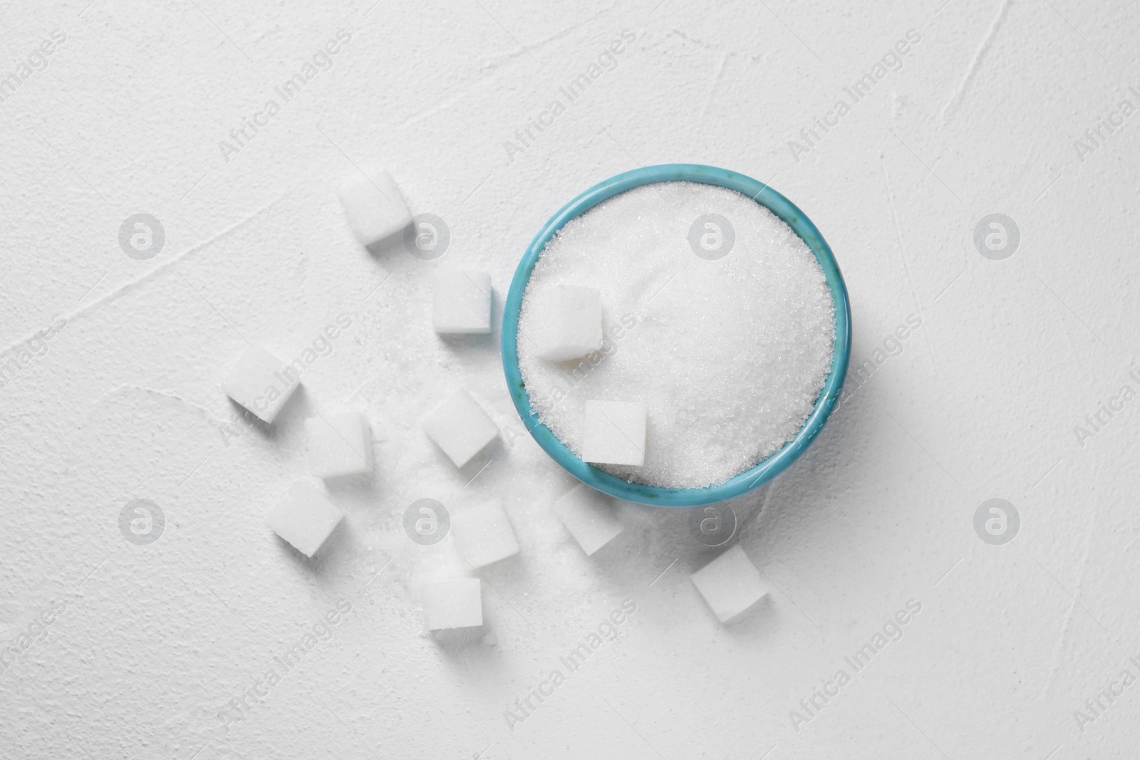 Photo of Different types of sugar in bowl on white table, flat lay