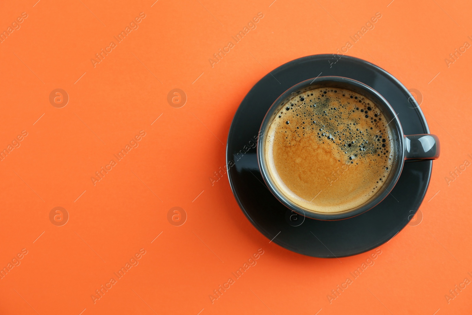 Photo of Cup of tasty coffee on orange background, top view. Space for text