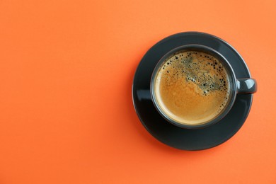 Cup of tasty coffee on orange background, top view. Space for text