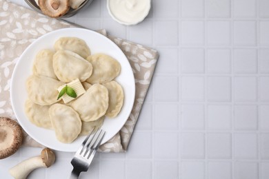Delicious dumplings (varenyky) with mushrooms and butter served on white tiled table, flat lay. Space for text
