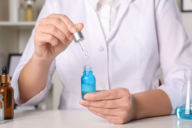 Photo of Dermatologist developing cosmetic product at white table indoors, closeup