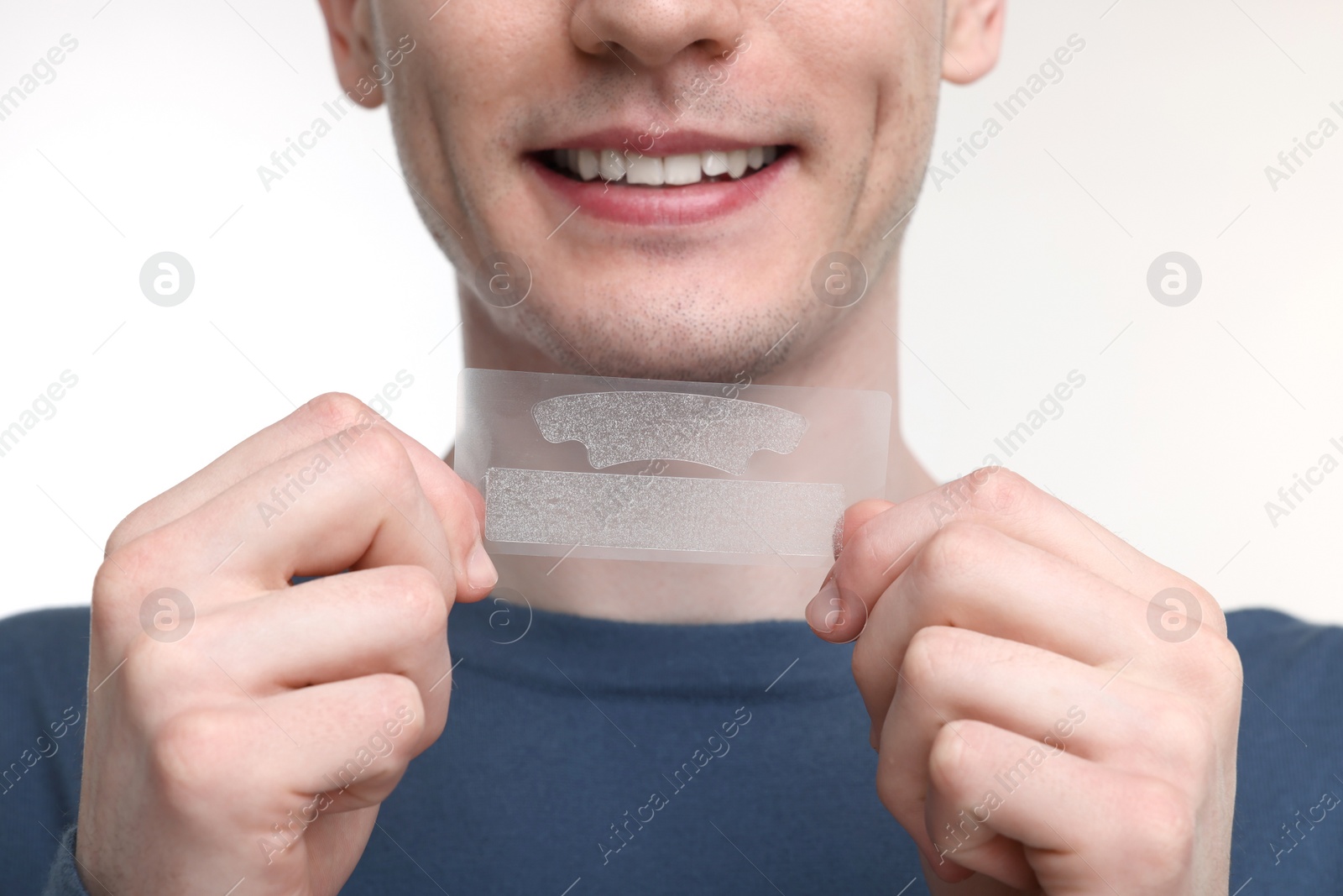 Photo of Young man with whitening strips on light background, closeup