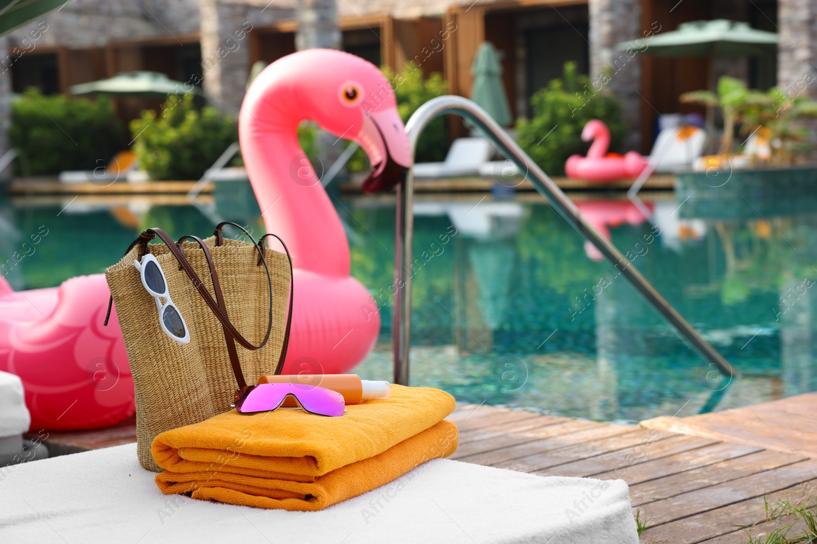 Photo of Beach accessories on sun lounger and float in shape of flamingo near outdoor swimming pool, space for text. Luxury resort