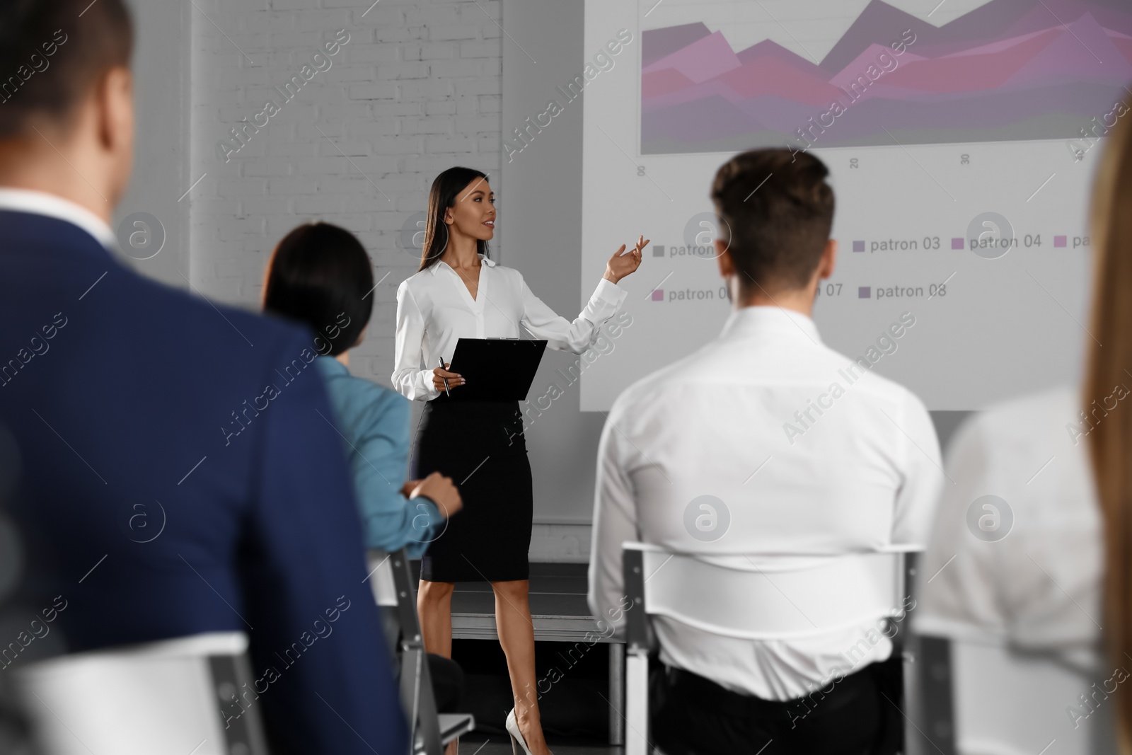 Photo of Female business trainer giving lecture in conference room with projection screen