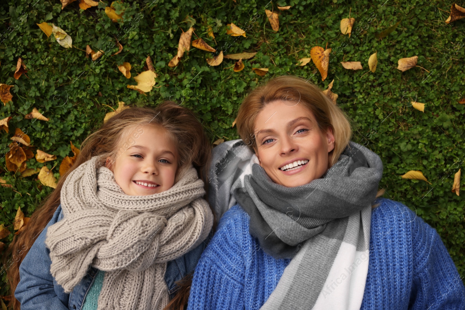 Photo of Portrait of happy mother and her daughter on green grass with autumn leaves outdoors, top view