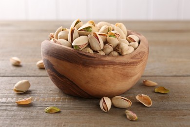 Photo of Tasty pistachios in bowl on wooden table, closeup