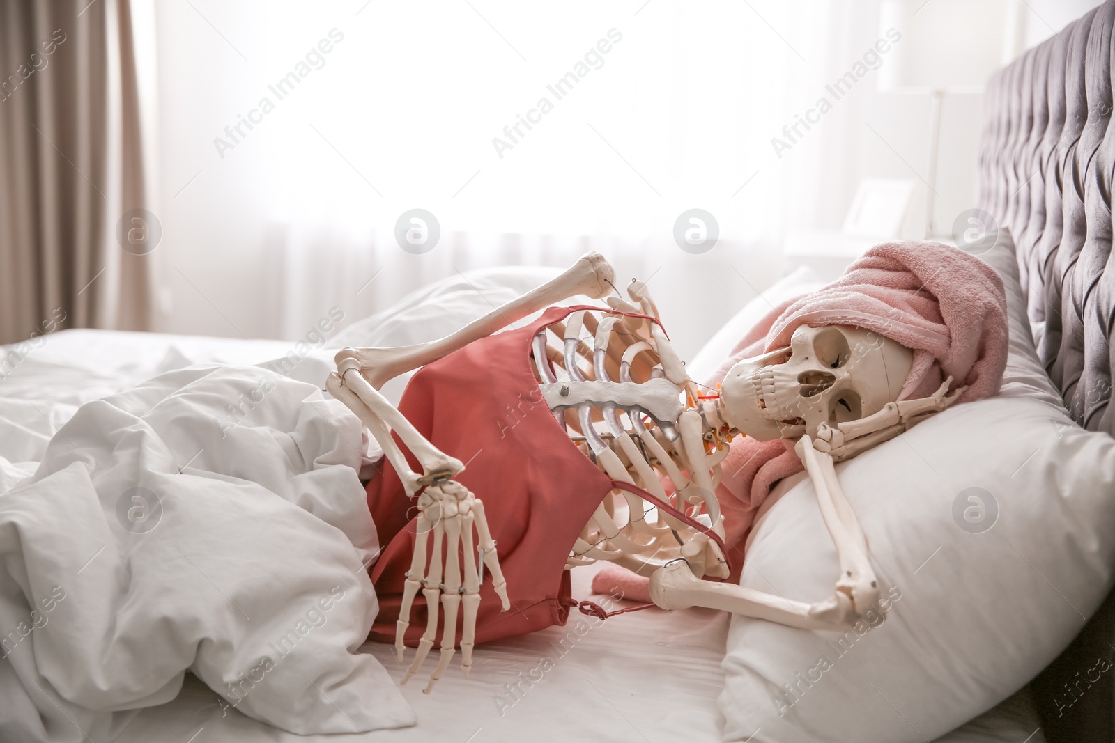 Photo of Human skeleton in silk pajamas and towel lying on bed indoors